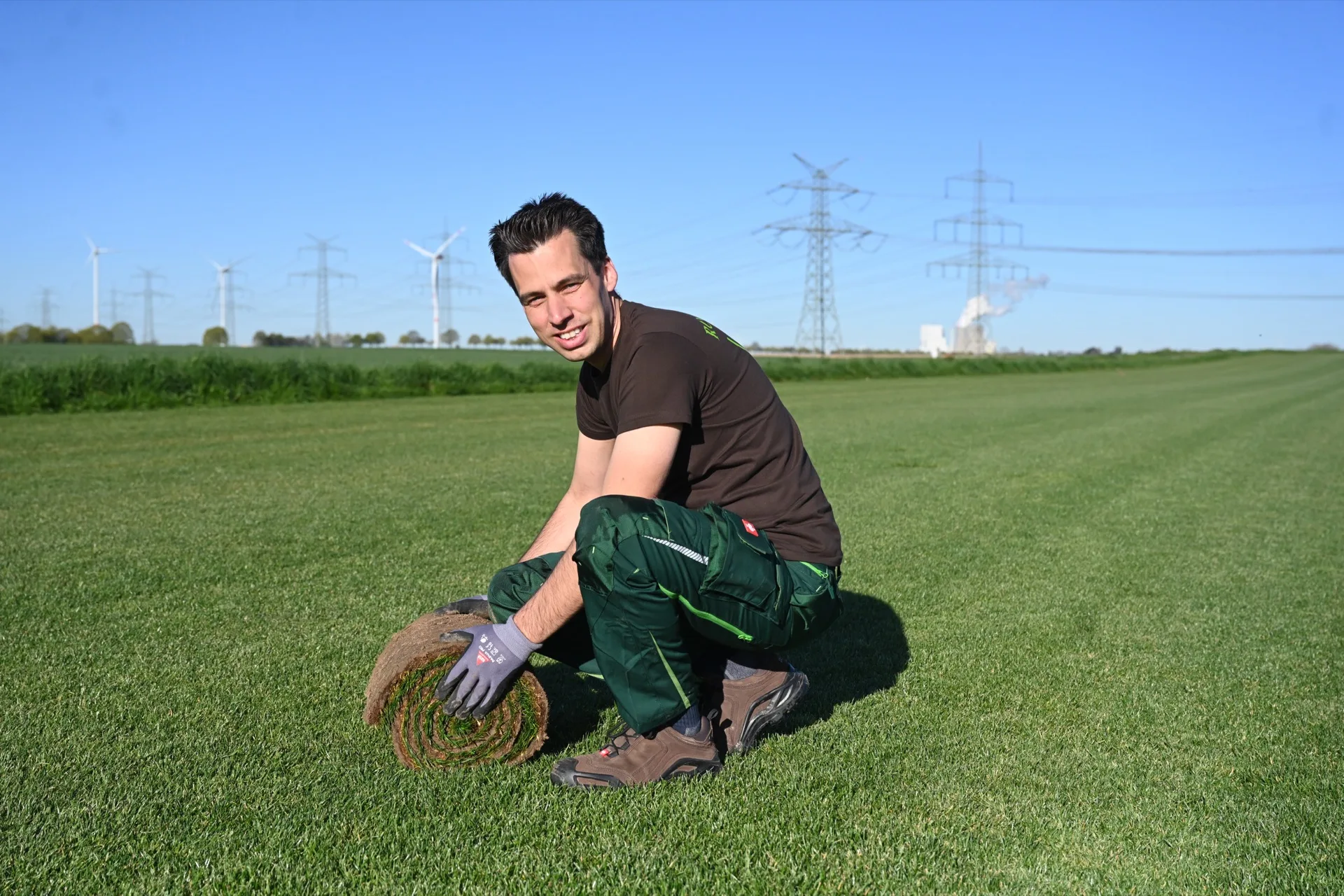 Thomas Decker mit einer frischen Rolle Premium Sport Rollrasen vor sattgrüner Rasenfläche